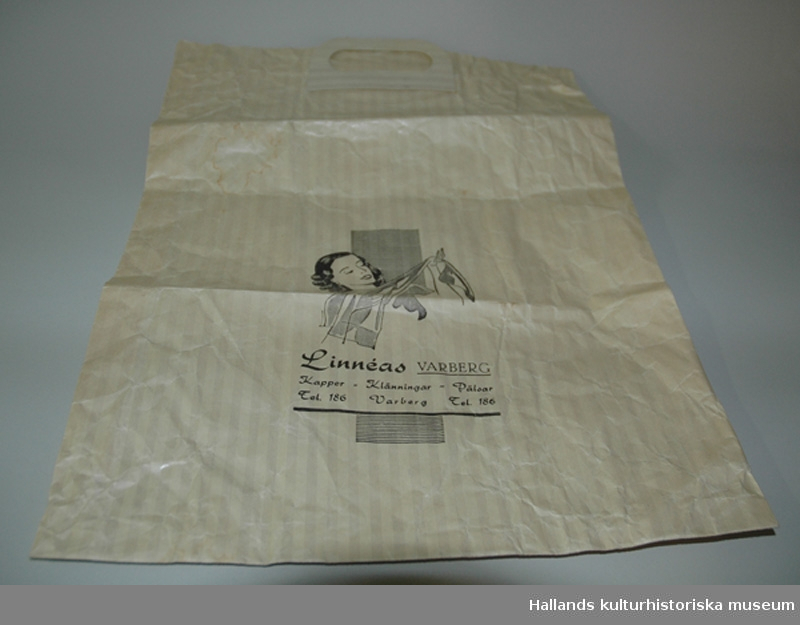 Påse av papper, handtag av papp. På ena sidan tryckt i svart:"Linnéas VARBERG kappor - klänningar - pälsar Tel. 186 Varberg Tel 186", samt bild av en kvinna, hållande i en silkesstrumpa.Höjd: 44 cm. Bredd: 33,5 cm.