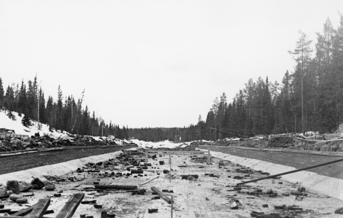 Fra anleggsområdet der det i perioden 1936-1938 ble reist en ny reguleringsdam ved elva Søndre Osas utløp fra Osensjøen i Åmot kommune i Hedmark. Dette fotografiet ble tatt tidlig i april 1937, antakelig i det som skulle bli et nytt damløp. Her hadde man bygd et golv og skrå sidevegger av planker, sannsynligvis for å lage en passasje der det var liten fare for at fløtingstømmeret skulle sette seg fast. Da bildet ble tatt lå det fortsatt mye kapp og annet avfall fra byggeprosessen på golvet.