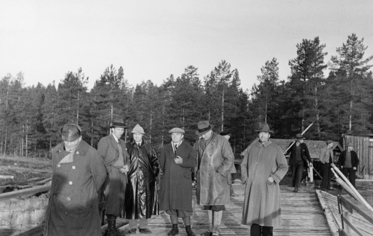 Direksjonsbefaring på Haldammen i Våler, Hedmark, i mai 1934. Bildet er tatt på dambrua, der seks menn - antakelig tillitsvalgte i Christiania Tømmerdirektion - poserte i forgrunnen. Til høyre i bakgrunnen skimter vi tre lokale fløtere. Vi ser også den ene av de to damkoiene ved Haldammen. I 1934 besto direksjonen - styret - i Christiania Tømmerdirektion av godseier Westye Parr Egeberg, disponent Cæsar Bang, direktør Hans Th. Kiær, tømmersjef Trygve Eng, overingeniør Axel C. Andersen, disponent Hans Høibraaten, disponent Olaf T. Messelt og skogeier Olav Nergård. Kaare Sparby var fløtingsinspektør i det distriktet direksjonen besøkte. Det er nærliggende å anta at flere av de nevnte personene er med på dette fotografiet.
