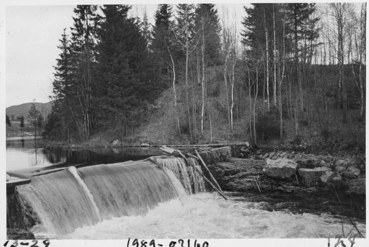 Ånebydammen i Nitelva i Nittedal kommune på Nedre Romerike, slik dammen så ut våren 1935. Bildet er tatt i motstrøms retning. Dette ser ut til å ha vært en terskeldam, altså en konstruksjon som skulle heve vannspeilet i den umiddelbart ovenforliggende delen av vassdraget. Her et det ett løp med et fall som kan se ut til å ha vært anslagsvis en meter høyt. På begge sider av damløpet er det støpte murer. I bakgrunnen, ved venstre bildekant, ser vi et toetasjes kvitmalt bolighus med veranda mot vassdraget. I 1935 ble det innmeldt 34 304 tømmerstokker til fløting i Nitelva.