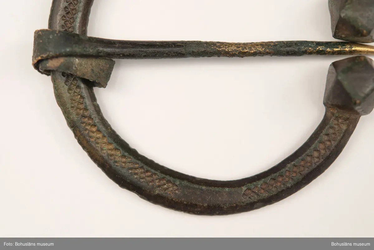 Hästskoformat ringspänne av brons, med dekor. En tillplattad rund bygel med fasetterade ändknoppar. Dekoren består av instämplade romber ovanpå bygeln. Nålens fäste är utplattad och upprullad runt bygeln.

Ringspännet är troligen från vikingatid, år 800-1050 e Kr. och användes för att hålla samman klädedräkten, exempelvis ett ytterplagg, en mantel, vid halsen. 

Citat ur brev som medföljde gåvan: "Brosch från bronsåldern - hittad av David Leonard Thorburn i jorden. Var?" (ur Agnes Thorburns anteckningar). 
Enligt Agnes bror, Thomas Thorburn, påträffades den troligen någonstans i Uddevallas omgivningar. David Thorburn var, enligt honom, känd bland bönderna som en person som köpte kuriosa. Thomas Thorburn skulle därför tro att någon bonde hittat den och sålt den till David Thorburn."