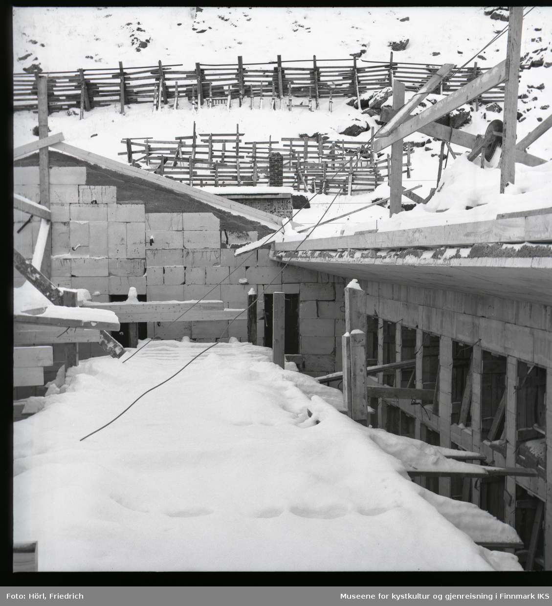 Bildet er tatt fra et stillas som står i råbygget til den katolske kirka St. Mikael i Hammerfest i vinteren 1957 /1958. Det er tatt i retning Salenfjellet der det er satt opp snøgjerder som til dels virker provisorisk.