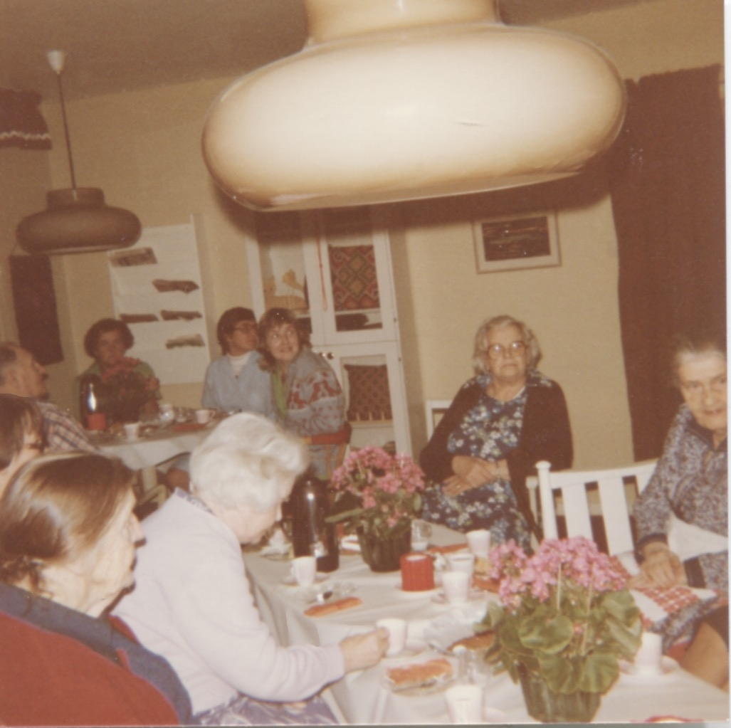 Personal och boende sitter och fikar i Brattåshemmets terapirum på nedre våningen, 1970-tal. Namnuppgifter saknas. I blå rock sitter en kvinnlig personal.