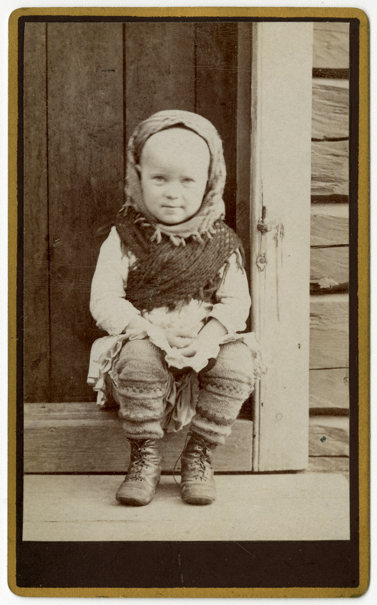 Foto av liten jente i dørkarm. Anna Bjørnsmed (?) Utydellig påskrift, kan leses i albumside