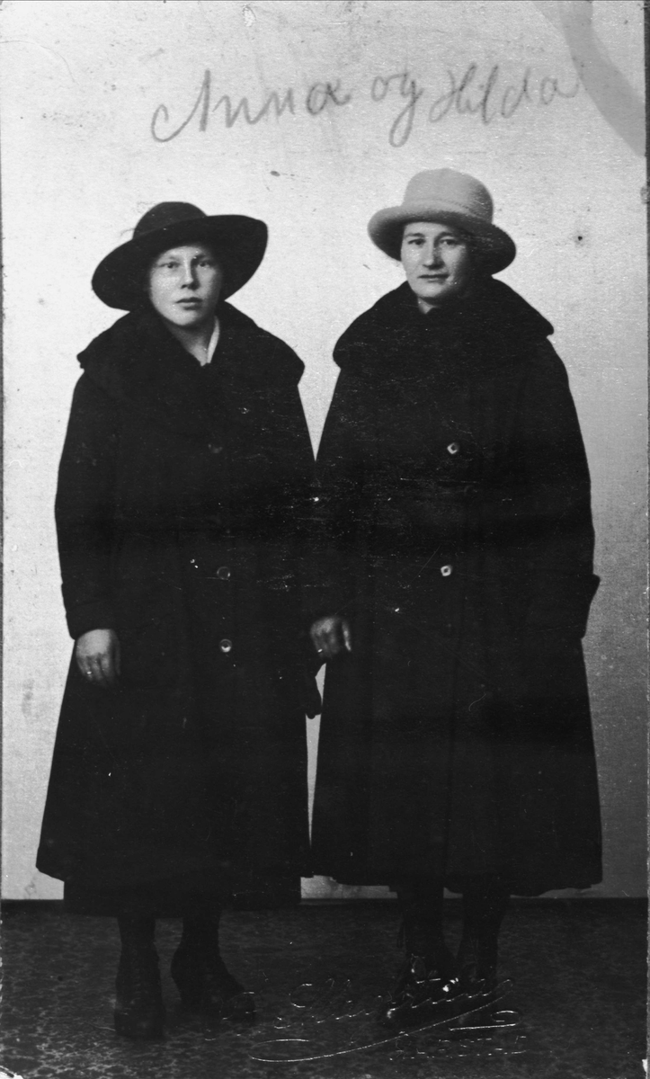 Studioportrett av to kvinner i helfigur med kåpe og hatt.