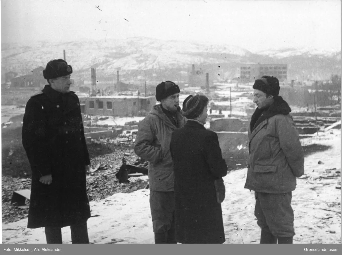 Tre sovjetiske soldater, muligens offiserer, i samtale med en eldre kvinnelig sivilist i ruinene av Kirkenes by. Bildet er tatt enten på høst-vinter i 1944 eller på vinteren i 1945.  