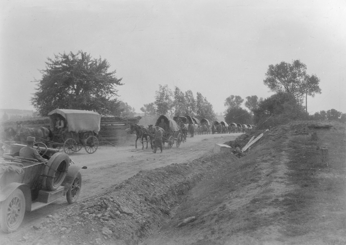 13 hästekipage med vagn och militärer samt en bil på en väg vid militäranläggning under första världskriget. Tillhörande Österrike-Ungern.