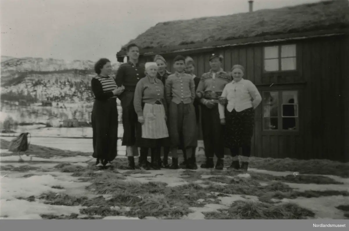 Åtte mennesker står foran et hus. Husmannsplass i Valnesfjord.