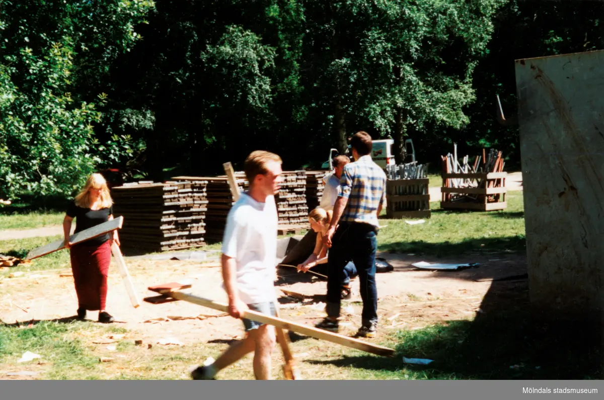 Sommarspelet/barnteaterföreställningen "Rasmus på luffen" 1999 vid Byxorna i Gunneboskogen (korsningen Christina Halls väg/John Halls väg). Kvinnor och män går omkring med olika delar till teatern, troligtvis efter nedmontering.