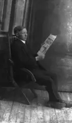 Studioportrett av ung mann som sitter i en stol og leser en 