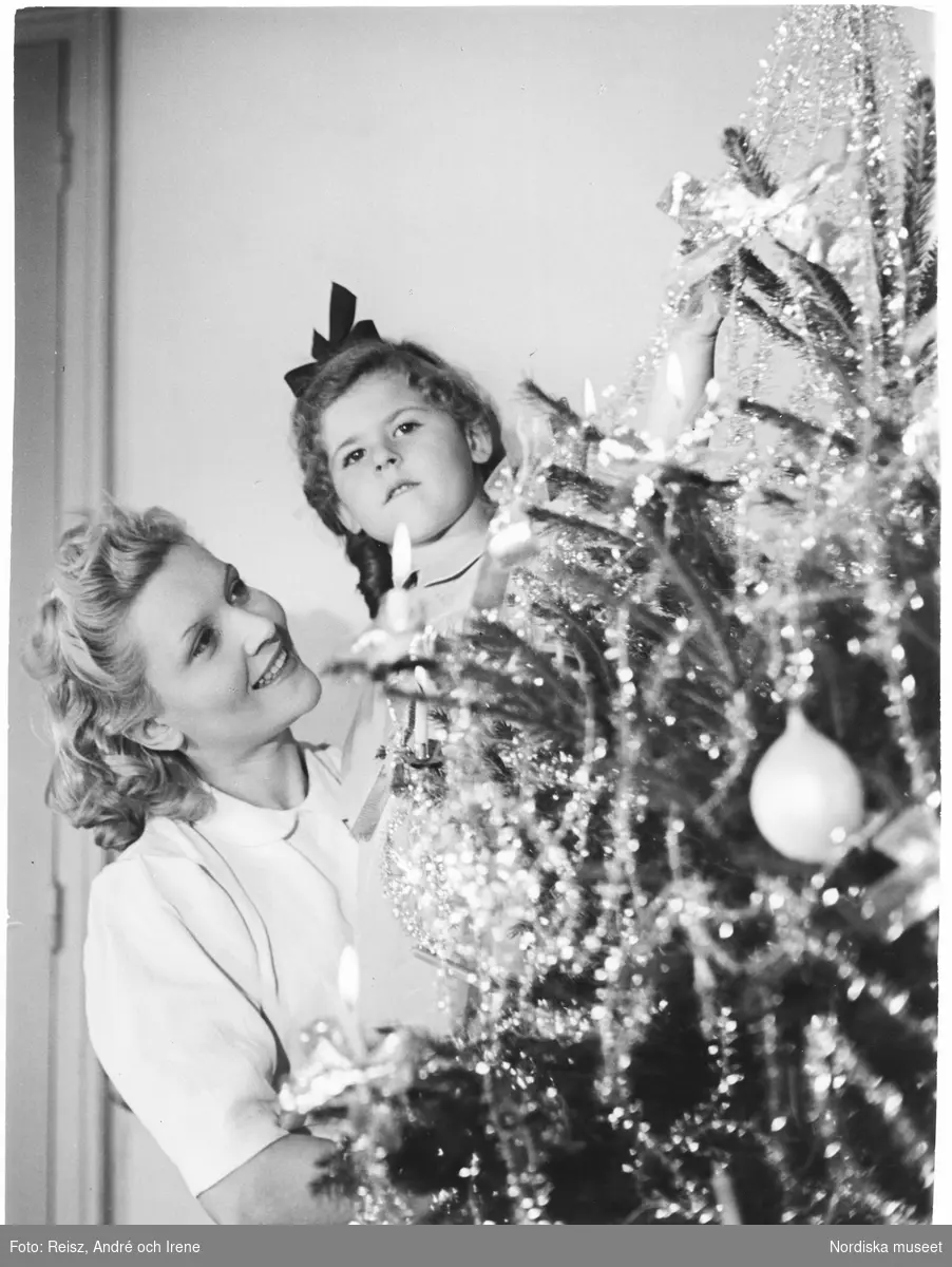 Jul. En kvinna lyfter upp en flicka till julgranen.