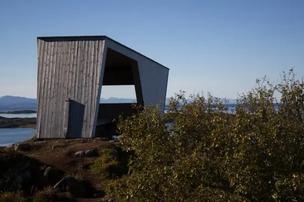 Moderne gapahuk på bakketopp med sjå og holmer i bakgrunnen.