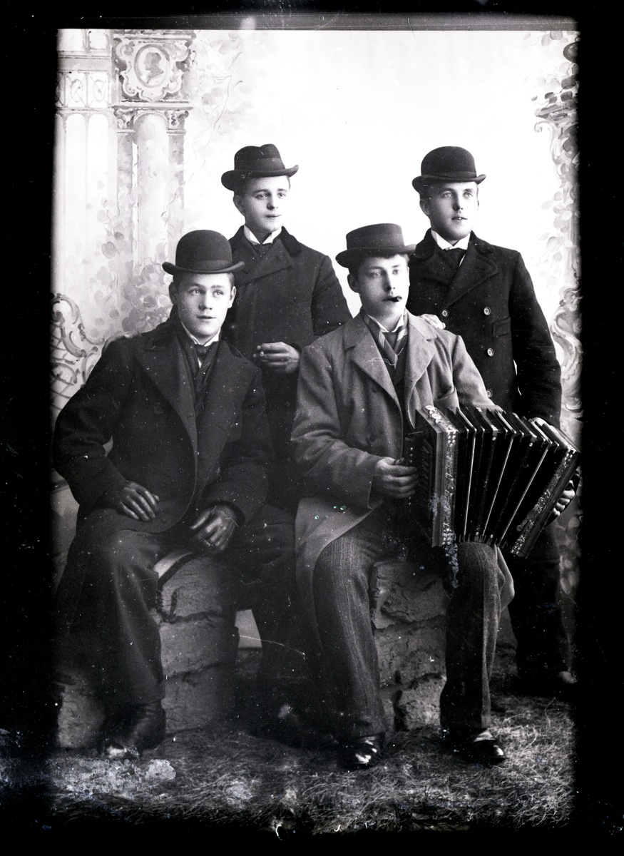 Atelierfoto. Fire yngre menn med hatter, en mann holder et trekkspill.