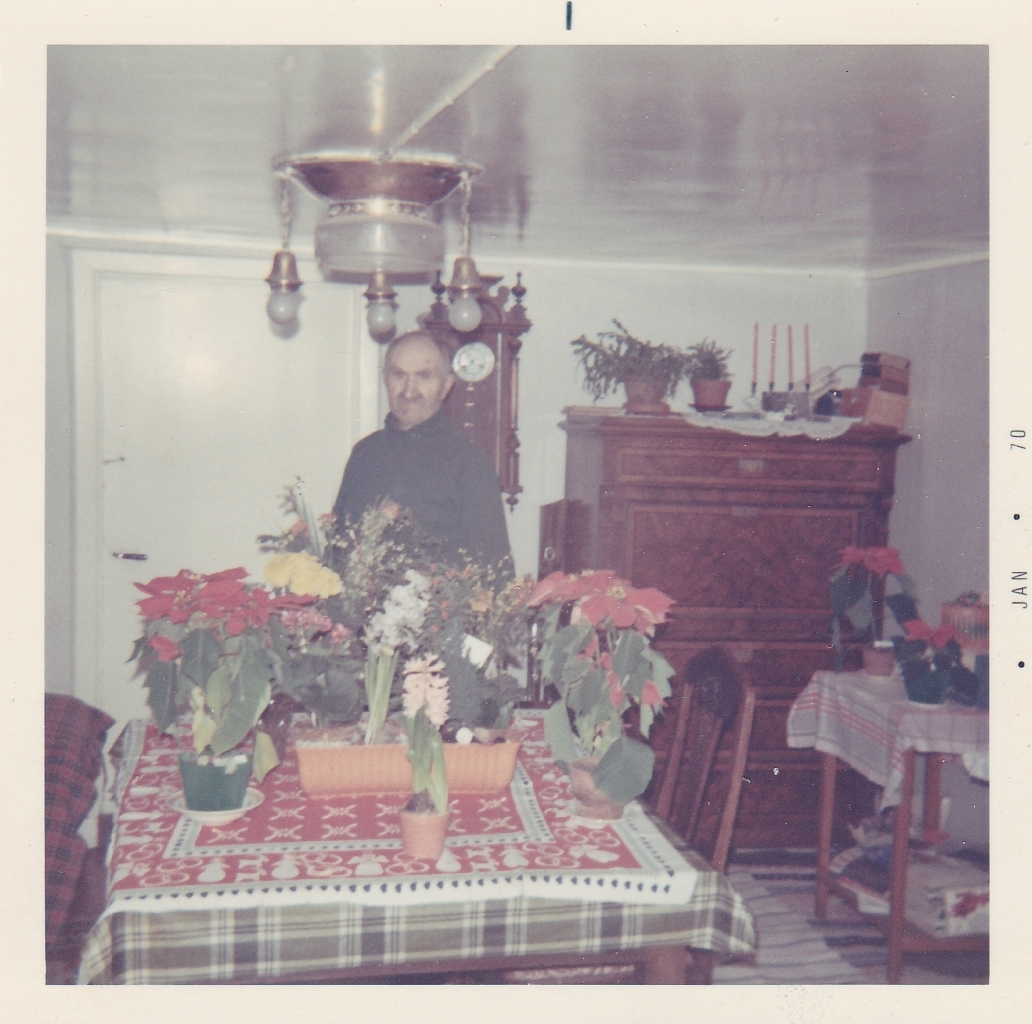 Uppvaktning för David Bengtsson (1889 - 1977), Långåker 1:2, januari 1970. David står bakom ett bord som är fyllt av blommor. Ett väggur och en sekretär skymtar i bakgrunden.