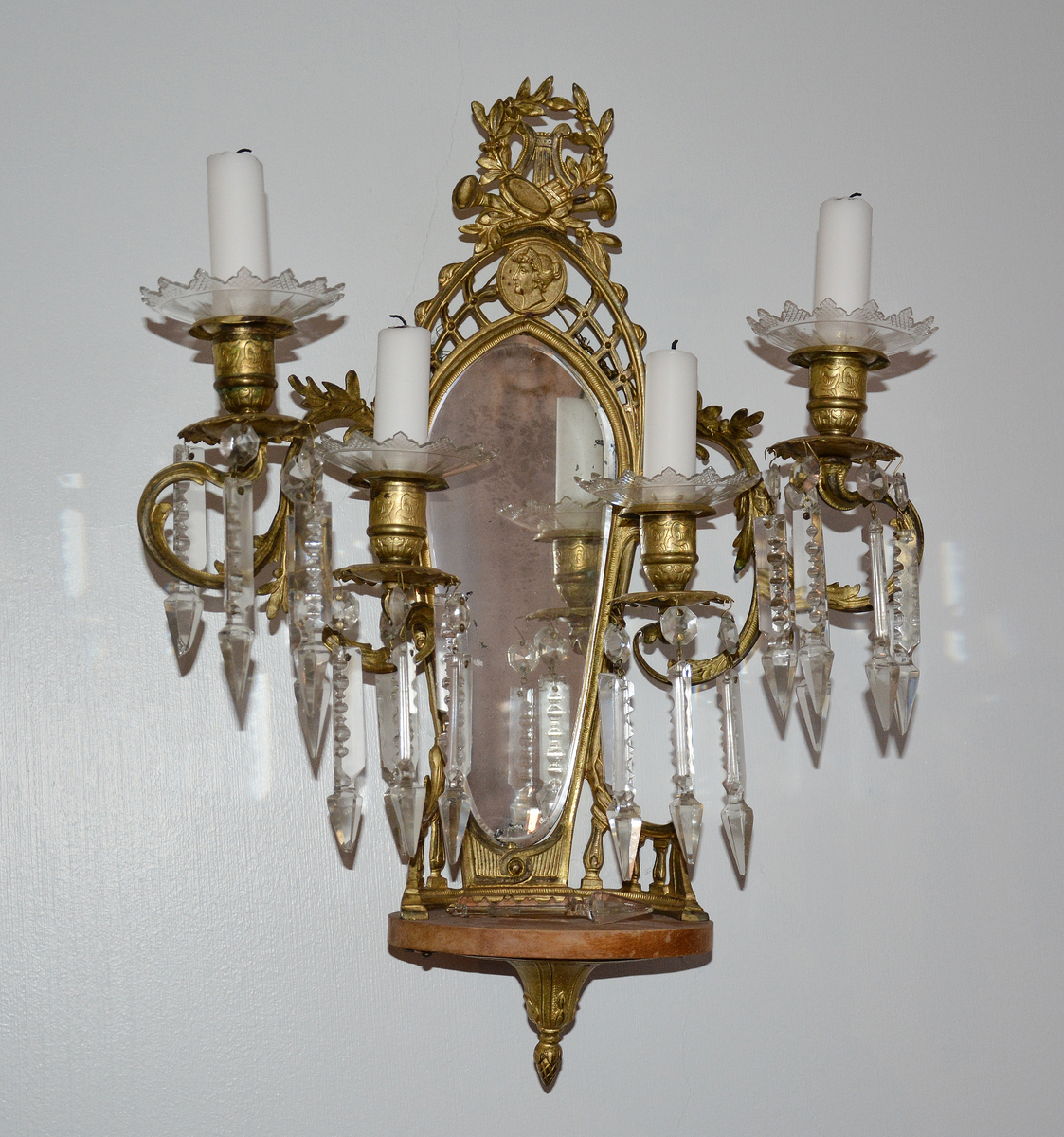 Lampett med fire armer, prismer, dryppskåler i glass, speil og lite konsoll.

