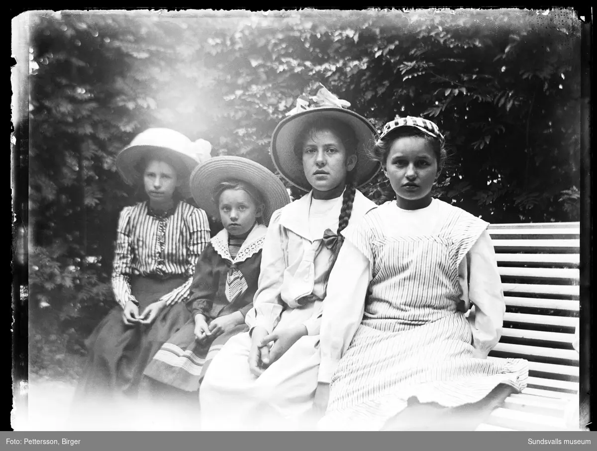 Porträttbild med fyra flickor som sitter på en bänk i en trädgård eller park.