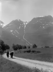 Mann og hest langs en landevei. I bakgrunnen ruver fjellene.