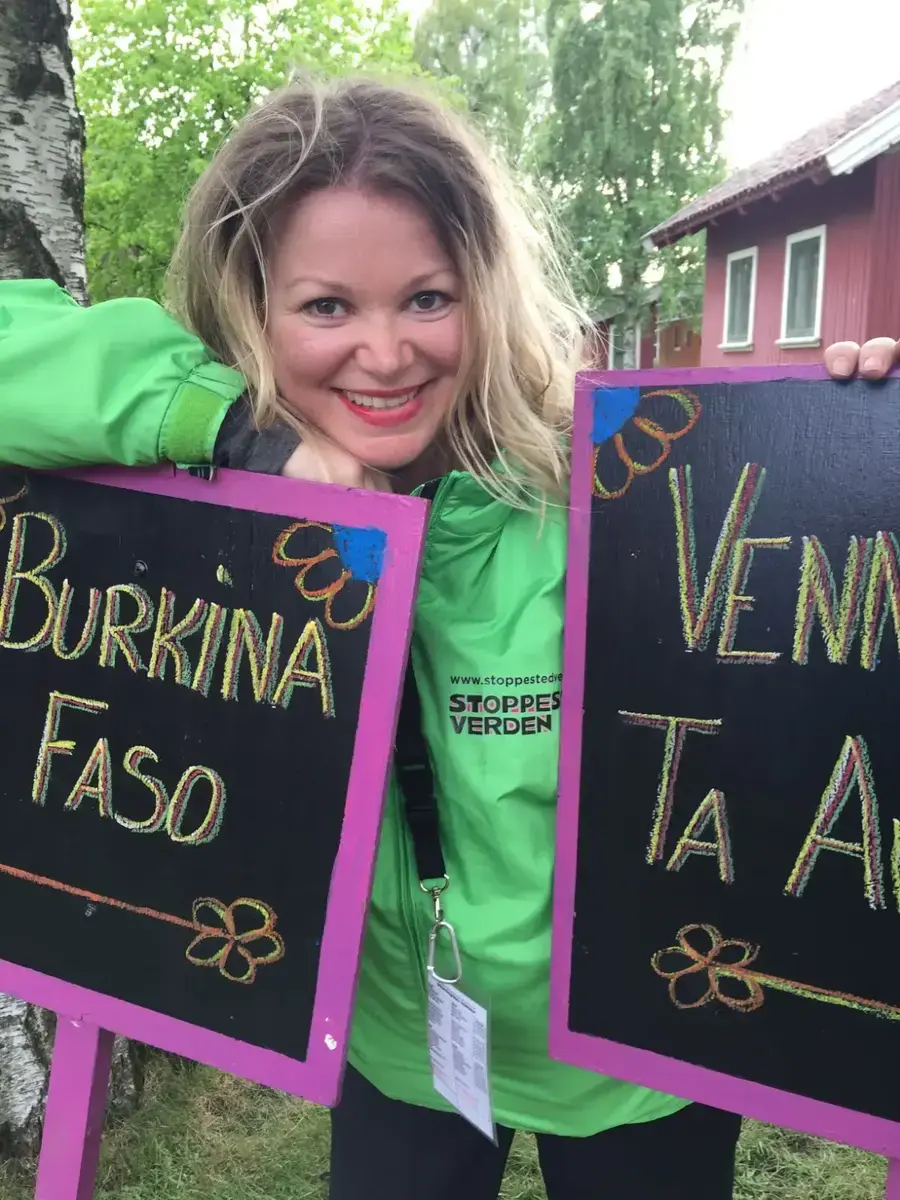 Kvinne i grønn jakke på festival som står med to skilt med navn på landene Burkina Faso og et man ikke ser navnet på.