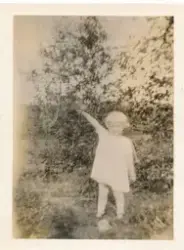 En jente står ute foran et tre og peker til venstre.