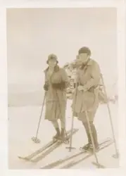 To kvinner står på ski på fjellet, bak dem er en varde og en