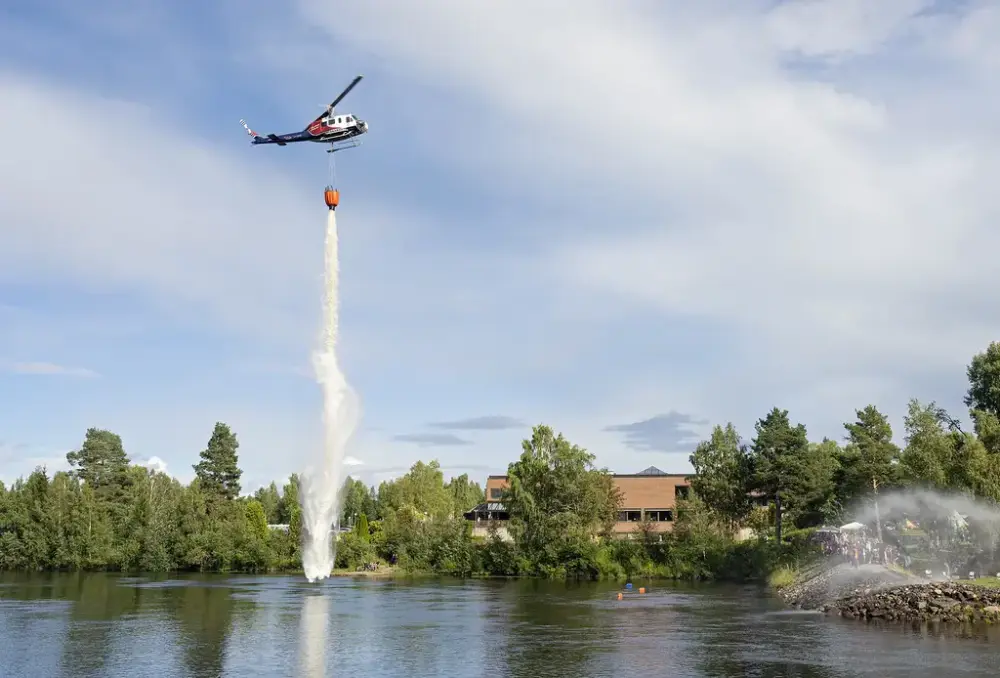 Helikopter med vanndunk svever utenfor skogmuseet. Det demostrerer brannslukking fra lufta. 