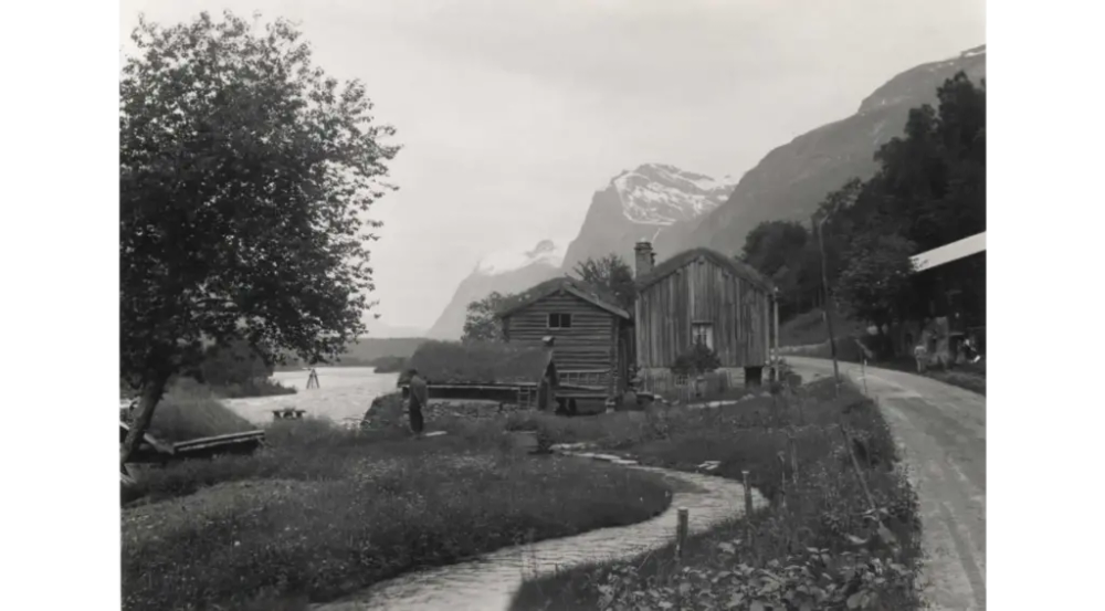 Gårdstun ved elva Driva med fjell i bakgrunnen, en vei går gjennom tunet.