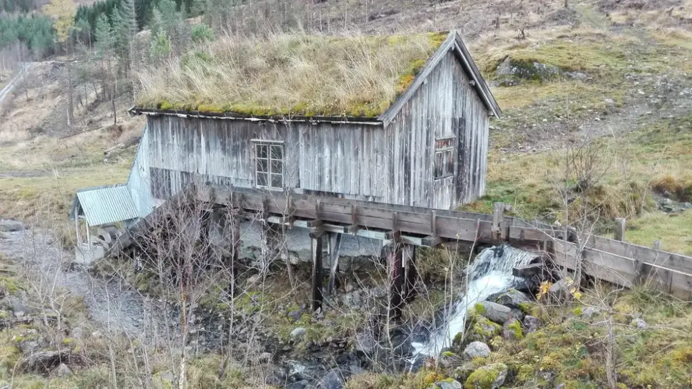 Trebygning med torvtak med vassrenne som leder til undervannshjul ved siden av bygningen.