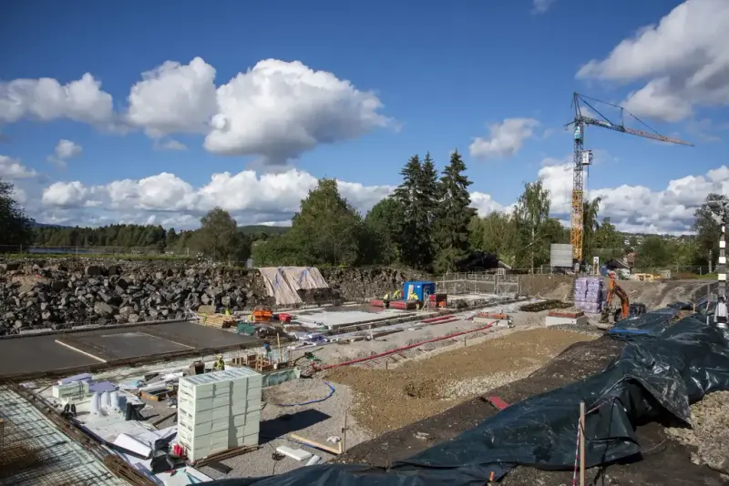 En del av grunnflata er støpt, noe mer er klargjort med markisolasjon og armeringsjern, og store stabler med mer isolasjonsplater står strategisk plassert mens byggekrana står i bakgrunnen.