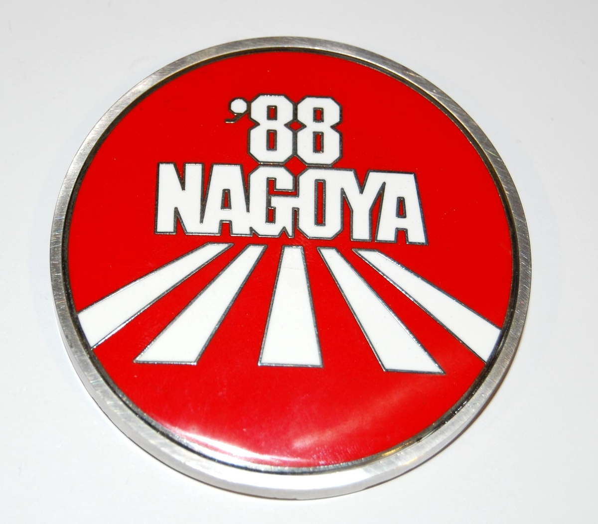 Rød, hvit og sølvfarget medalje med motiv av et type slott i Nagoya.


