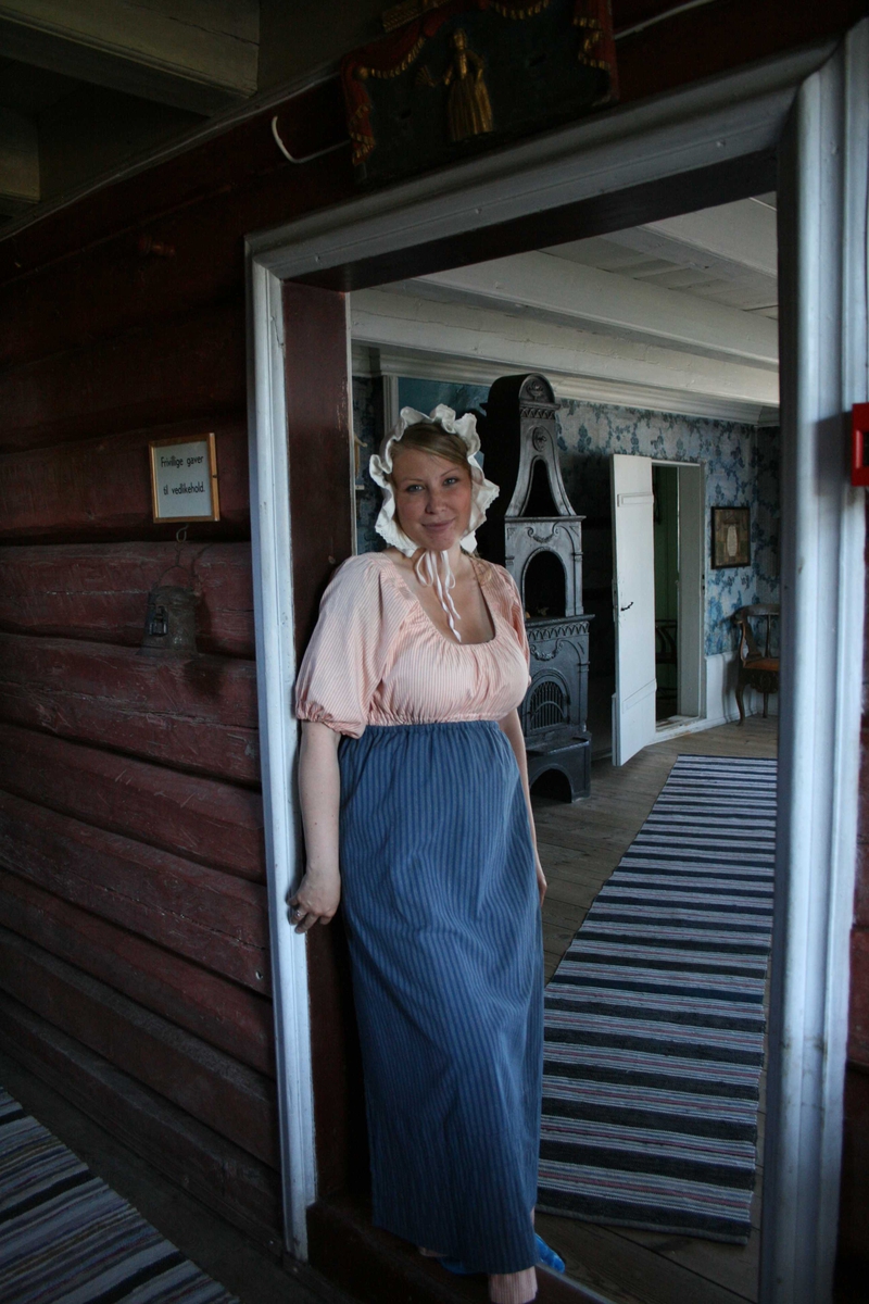 Museumsguide på Merdøgaard sommeren 2009. I døråpningen fra gangen til storstua. Kledd i kostyme som tjenestepike.