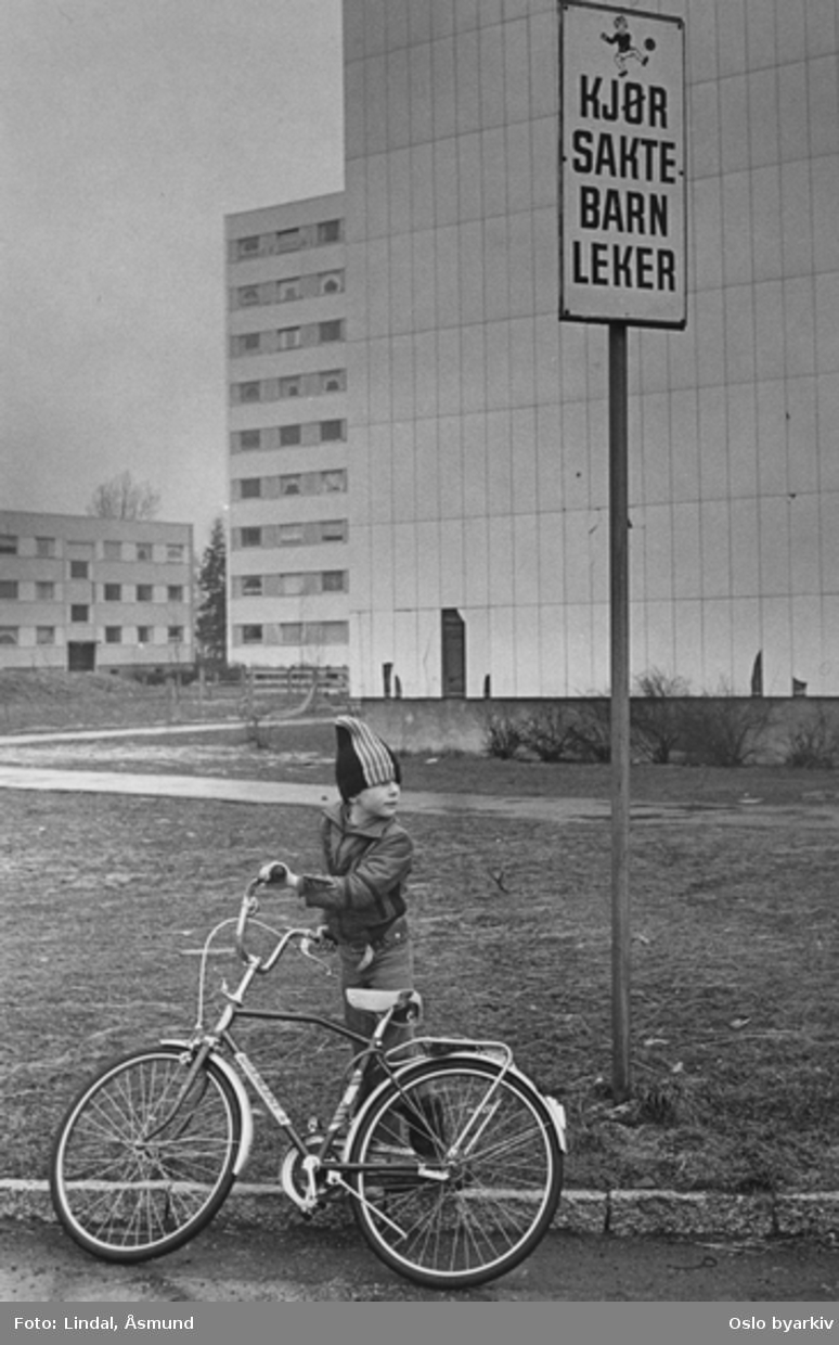 Gutt med sykkel foran høyblokk. Skilt: "Kjør sakte barn leker." Fotografiet er fra prosjektet og boka ''Oslo-bilder. En fotografisk dokumentasjon av bo og leveforhold i 1981 - 82''. Kontakt Samfoto ved ev. bestilling av kopier.