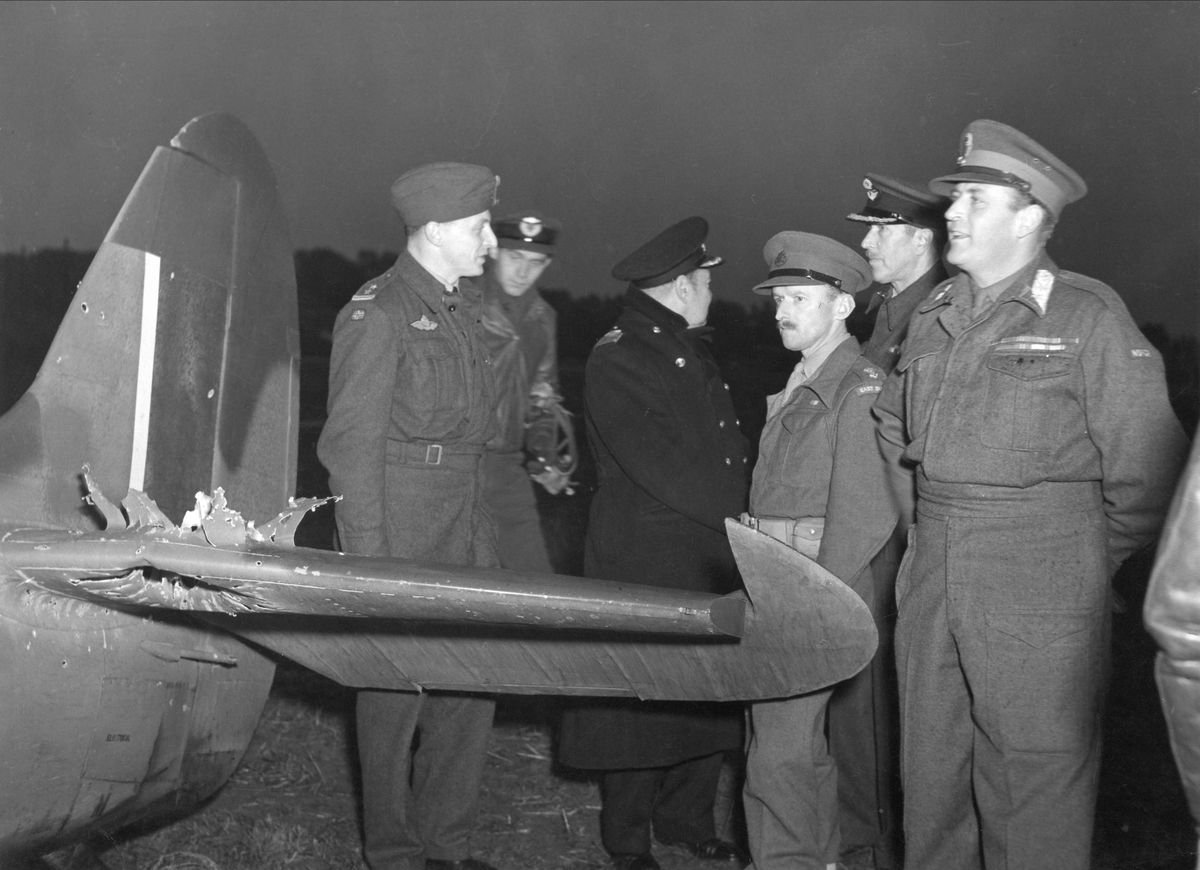 HKH Kronprins Olav på besøk hos en norsk jagerskvadron i Belgia. På bildet studerer han en Spitfire som har blitt truffet av tysk luftvernild.