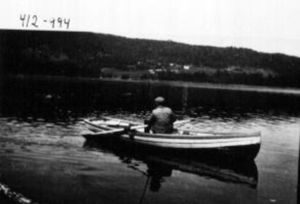 Fisketur på Mjøsa. Helge Henriksen med fiskestang i selvbygd robåt. Helgøya i bakgrunnen.
