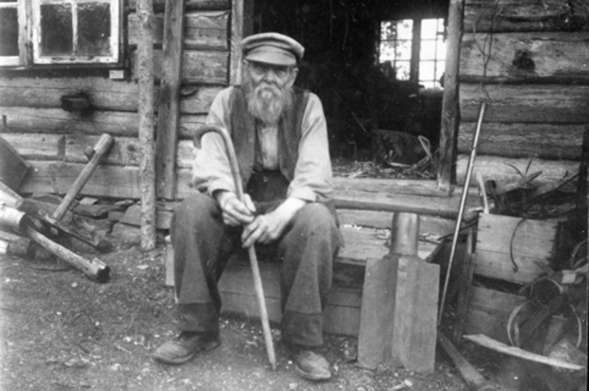 Snekkermester Hagbart Andreassen Lundstein (f 1861) sitter utenfor sitt snekkerverksted på Seilstad, Sandvold, Nes, Hedmark. Maler og utstyr fra verkstedet ble gitt til Domkirkeodden i 1973.