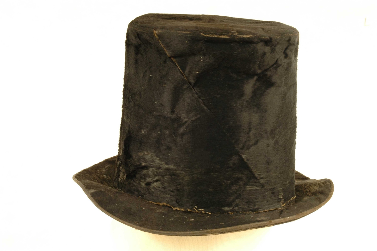 Svart flosshatt med høy pull og hatteband i svart bomull ved brem.