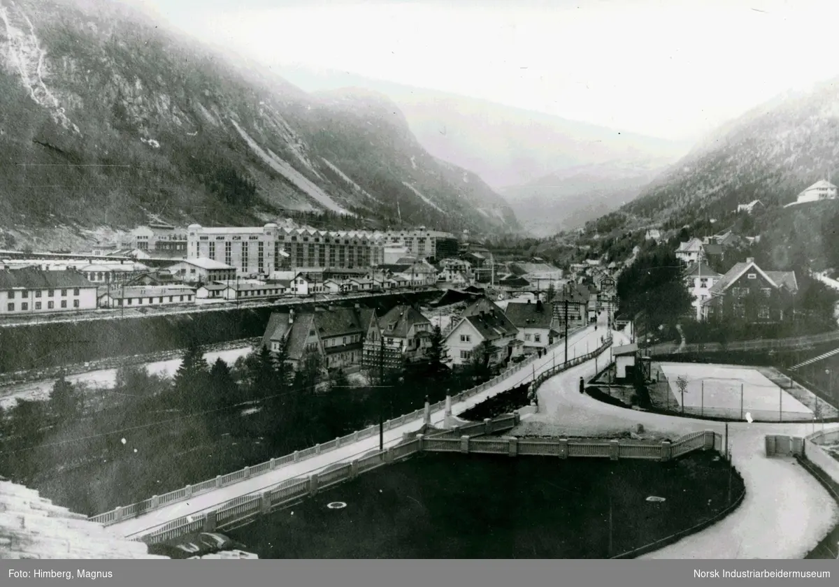 Fabrikkområdet på Rjukan etter utbygging tatt fra Sølvvolden i mai 1916. Tennisbanen tilhørende Adminiet sees til høyre. Boliger i Bråvold, Flekkebyen og Villaveien. Mennesker stående utenfor Rjukan Varelager.