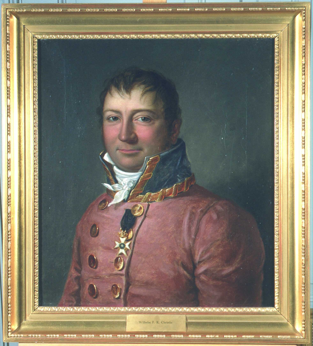 Portrett av sorenskriver Wilhelm F.K. Christie. Rød sorenskriveruniform, høy krave med gull, hvitt kalvekryss.  1 ordensstjerne.