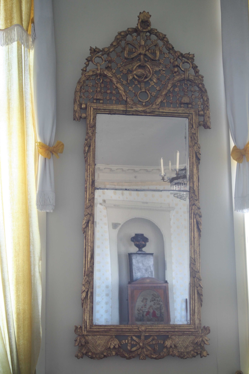 Louis XVI speil med delt glass.
Stor forgylt ramme med bladranker og gitter, papegøye i ring h. i sløyfe. ca. 1780 - 1800.