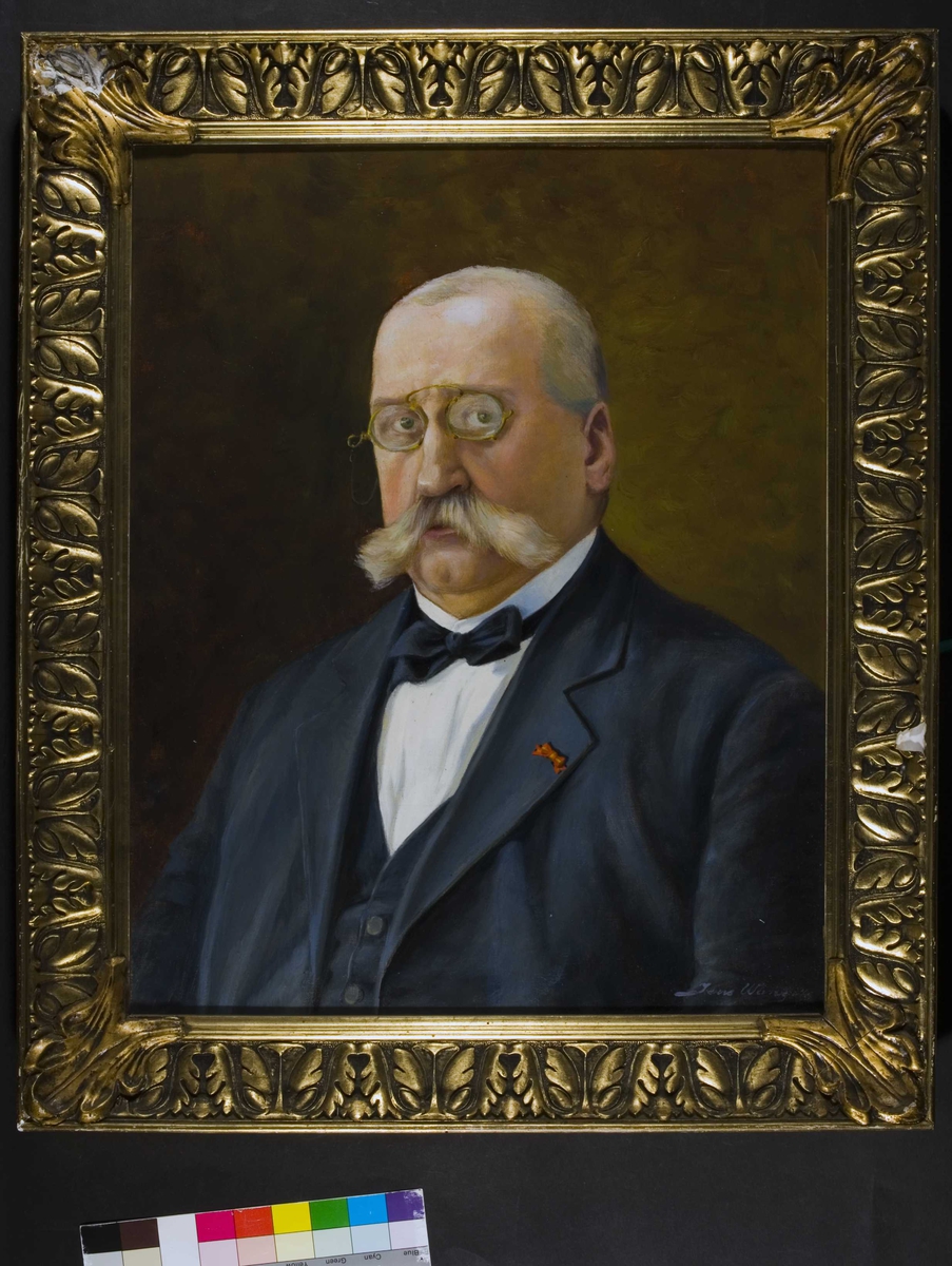 Portrett av Albert J Lange. Grått hår og bart, briller, mørk jakke og vest, hvit skjorte, sløyfe i halsen.