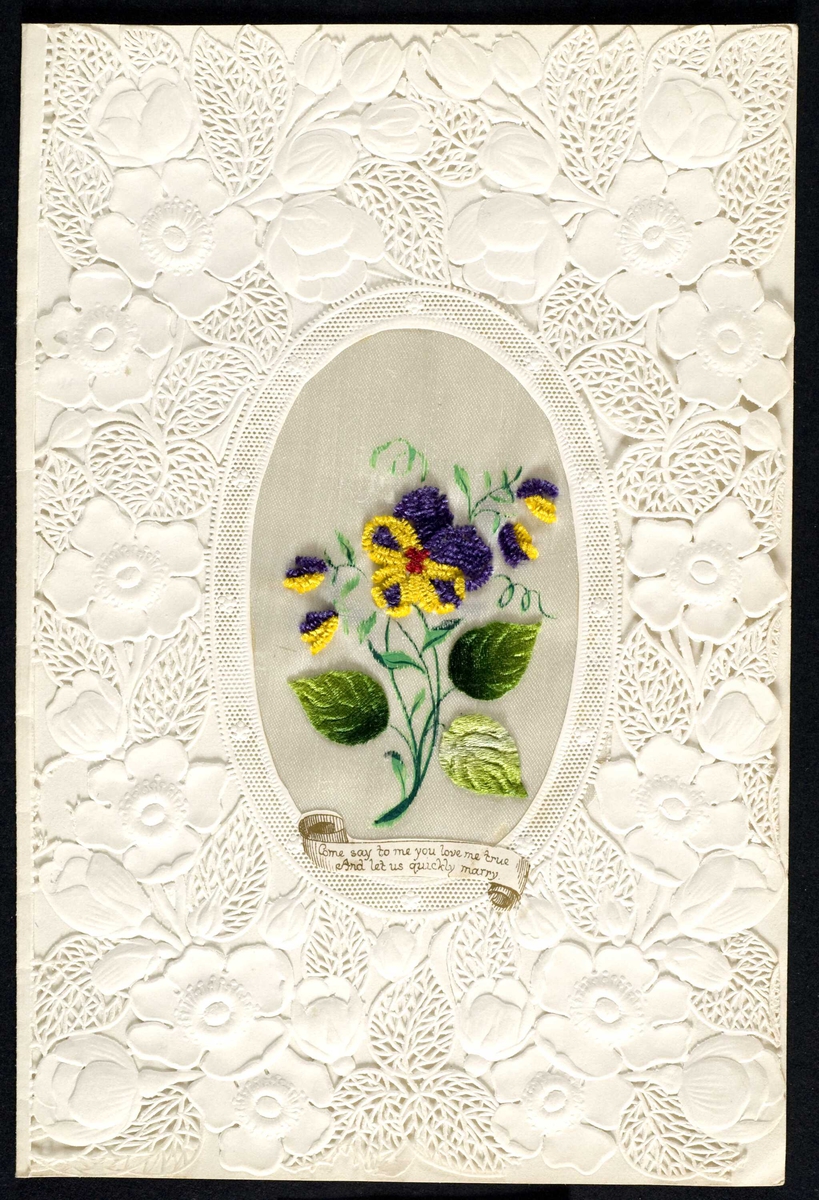 Ubrukt kort med pregede blomster og i midten en oval med en brodert blomst og liten trykt tekst.