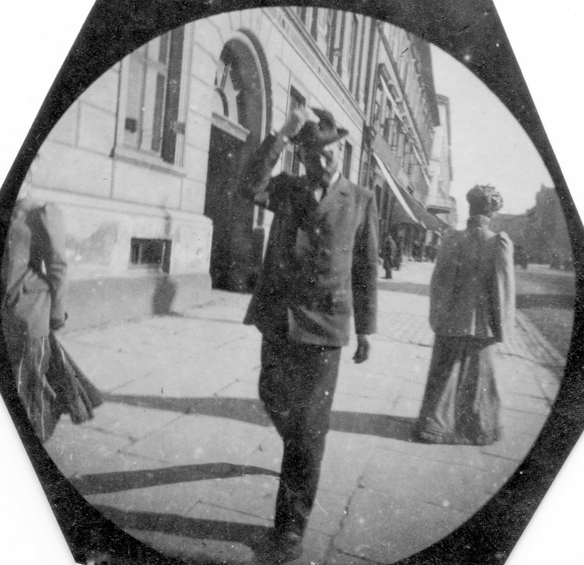 Adjunkt A. Andersen spaserer langs bygate, ant. Karl Johans gate, Oslo, med handa på hatten..