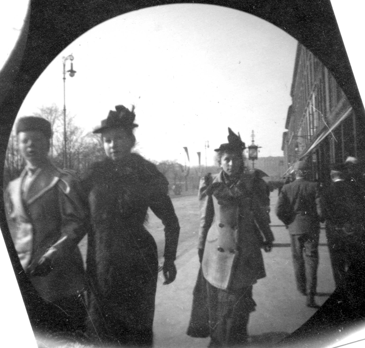 Tre kvinner spaserer på fortau langs Karl Johan, Oslo. To menn går i andre retningen. Bygårder.