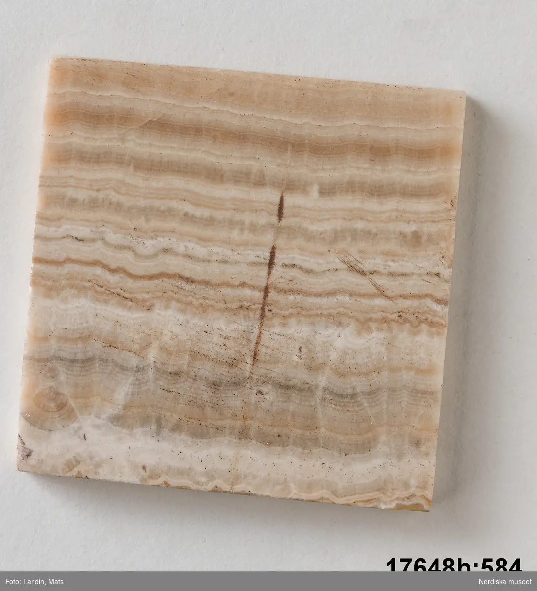 Kvadratisk platta av sten (trol. alabaster). Randigt mönster i olika bruna och vita nyanser. 
/Leif Wallin 2014-01-07