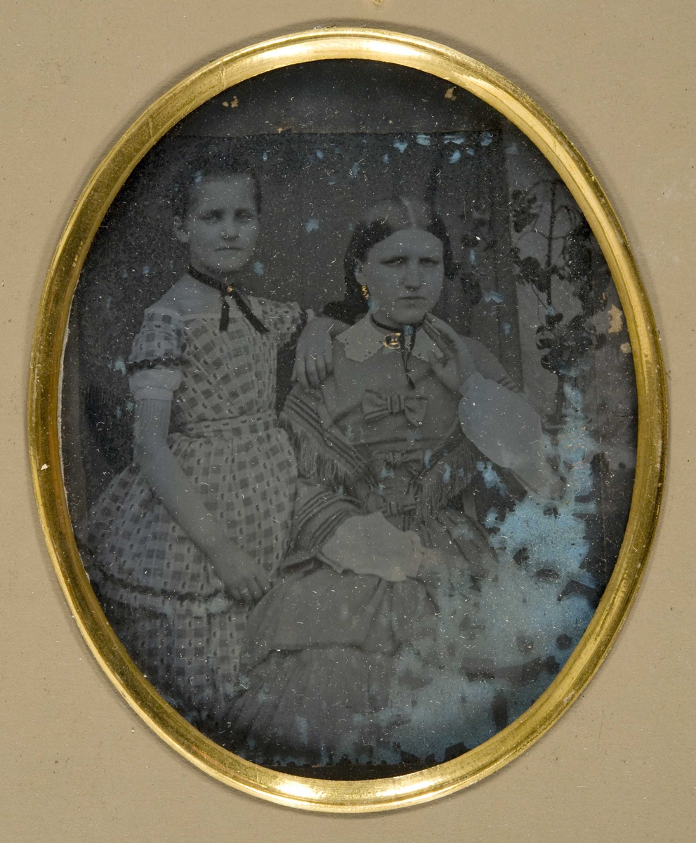 Portrett av kvinne og pike, Constance Aall, født Herlofson (1835-1897), gift 1859 med Jacob Aall (1833-1897), født på Nes Verk, Tvedestrand, Aust-Agder, med deres eldste datter, Augusta (født 1862). Mor sitter med støtte for venstre arm, datter står bakom, knebilde. 