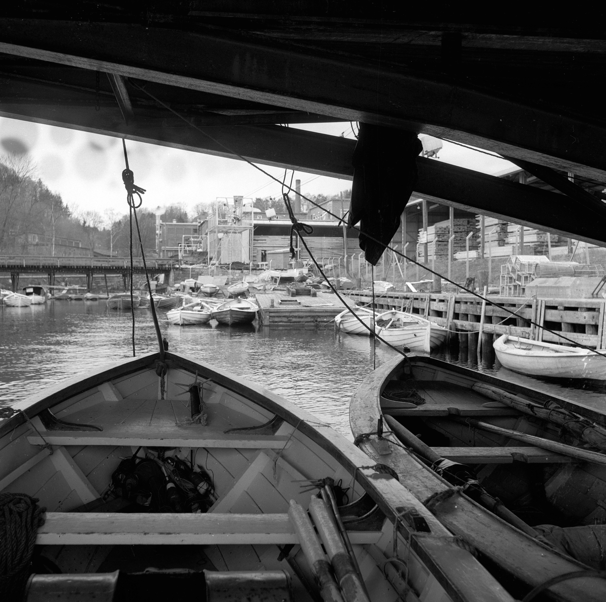 Trelastlager og båter på Farriselva i Hammerdalen, Riksvei 50. Fotografert 4. mai 1958.