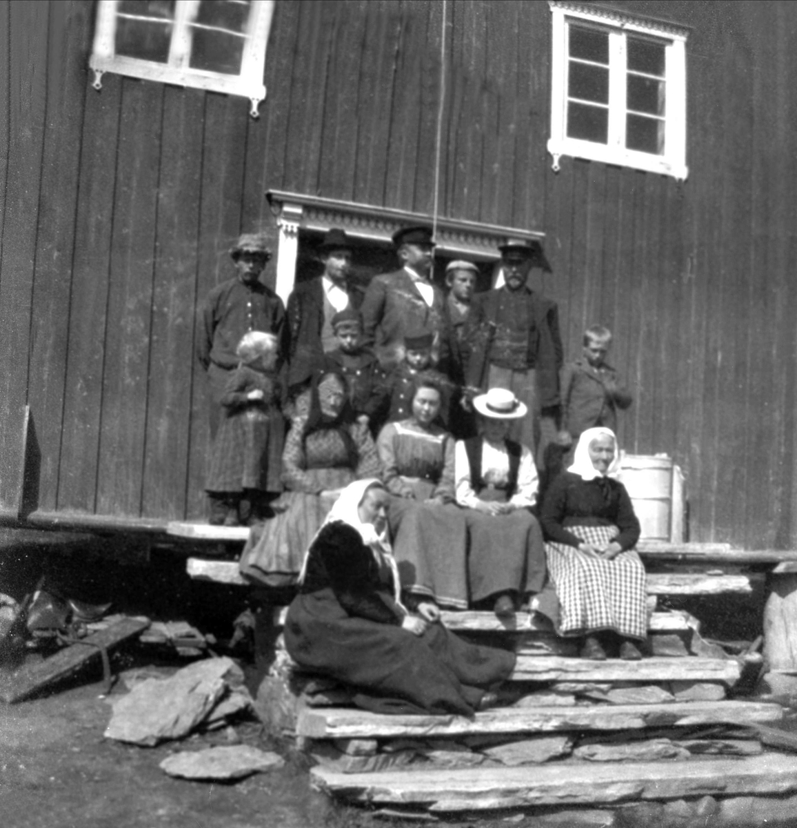Gruppe av voksne og barn på trappen til gammelt våningshus. I midten med lue på står Thorleif og Guri Arentz.