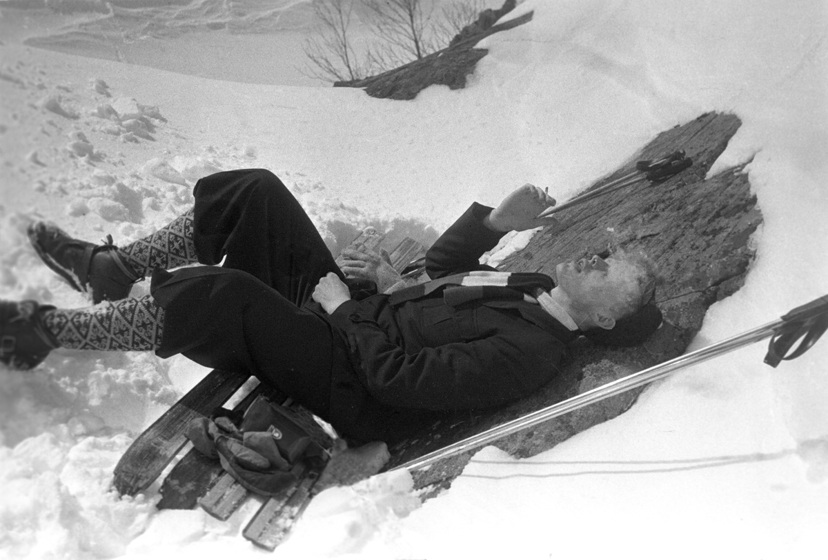 En person nyter en sigarett på en benk i solhellinga. Holmenkollrennene på Voss 1952. Fotograf Dagbladet