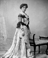 Portrett, kvinne i lys kjole med chiffonermer. Fru G Dahl.