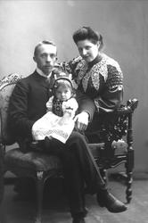 Gruppeportrett, mann og kvinne sitter med et barn på fanget.