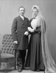 Gruppeportrett, brudepar. Bryllupsbilde, hun i svart kjole o